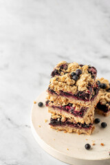 Stack of baked oatmeal squares with fresh blueberry on white tray on marble background with text space