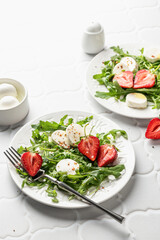 Salad with mozzarella with strawberries, mozzarella and arugula. Healthy light summer salad modern styling on white tile background text space