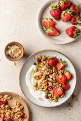 Healthy breakfast: fresh granola, muesli with yogurt, strawberry and honey on beige textured background. Top view
