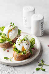 Poached egg sandwich with cucumber and microgreens. Healty breakfast bruschetta on white...