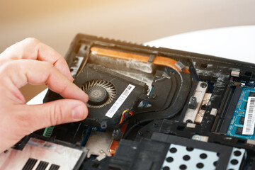 Fixing laptop. Repairman holds cooling fan and repairs from overheating. Disassembling computer, replacement, clean dust and dirt cooling system on notebook. Professional electronic device service