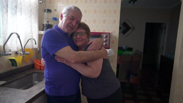 Senior couple loving embrace standing in home kitchen, causal authentic real life married man and woman hug, husband with arm around wife