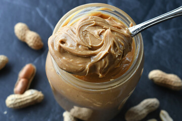 Selective focus of swirled peanut butter on a spoon on top of the peanut butter jar with no label. January 24 is National Peanut Butter Day