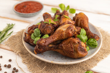 Smoked chicken legs on a ceramic plate on a white wooden background. Side view, selective focus.