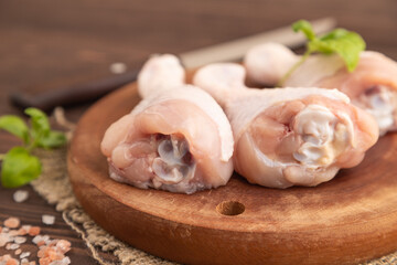 Raw chicken legs on a wooden cutting board on a brown wooden background. Side view, selective focus.