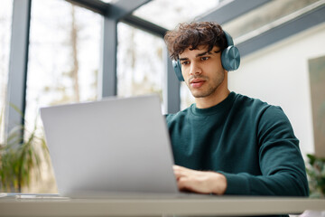 E-learning concept. Focused european guy in headphones looking at laptop, watching online lecture,...