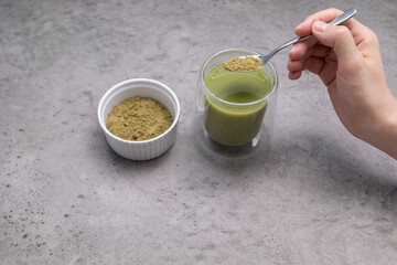 Human hand Adds Spoon of Hemp Protein Powder To Glass With Smoothie, Juice. Drink With...