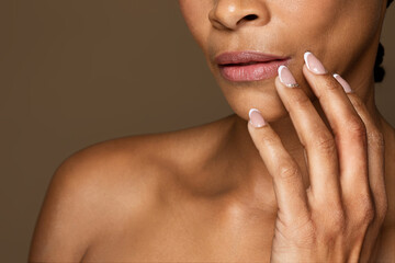 Closeup shot of black woman with flawless skin touching lips with fingers posing over brown studio...