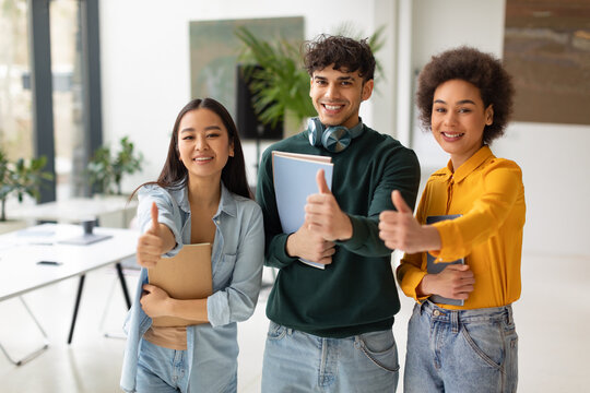 Happy diverse students gesturing thumbs up, standing in coworking space, approving their college educational program
