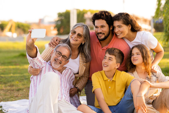Glad european multi-generation people enjoy picnic in park, taking selfie on phone