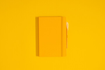 Top view of yellow notebook and pen on yellow background.