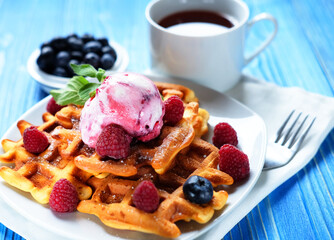 Waffles with ice cream and raspberries for breakfast over blue wooden table.