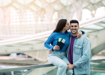 Joyful Woman Kissing Husband Holding Boarding Pass Tickets In Airport