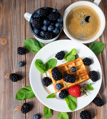Blackberry waffles with blueberries and a cup of coffee for breakfast, close up