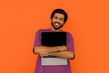 Positive indian man hugging laptop with blank screen on orange