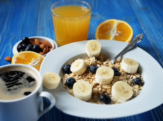 oatmeal with fresh berries, bananas on white plate with orange juice, blue wooden background.