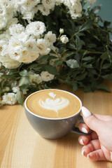 Coffee latte with female hand and flowers on cafe table
