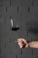 A glass of red wine in a man's hand against a dark gray brick wall