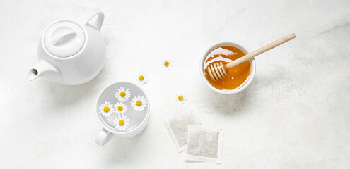 Teapot, cup of water, chamomile flowers, honey and tea bags on light background