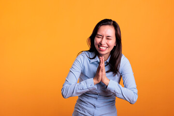 Cheerful filipino woman praying to god asking for forgiveness, posing with palms together in studio...