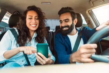 Navigation concept. Happy arab spouses driving car using smartphone and setting gps on phone