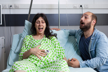 Pregnant woman having painful contractions, getting into labor in hospital ward while nervous husband yelling for doctor and medical assistance. Caucasian young couple preparing for childbirth