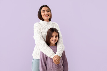 Little girl and her mother in warm sweaters on lilac background