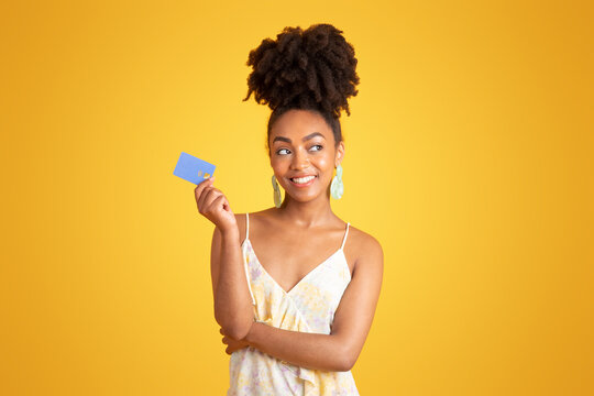 Cheerful pensive young black woman show credit card, dreaming about buying