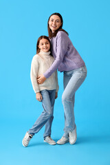 Little girl and her mother in warm sweaters on blue background