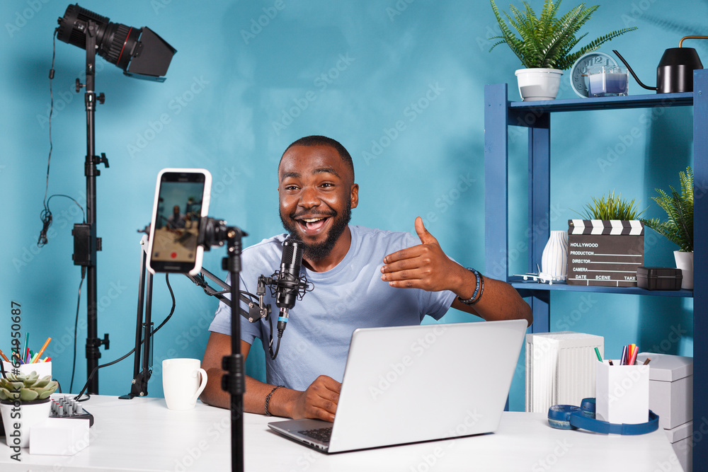 Poster african american blogger speaking and using laptop while recording video on smartphone for internet 