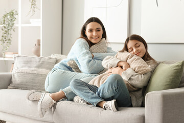 Little girl and her mother in warm sweaters with pillows sitting on sofa at home