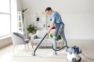 Male janitor hoovering carpet in living room