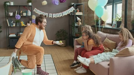Full shot of cheerful male entertainer in cat costume and makeup demonstrating party tricks with apple and cloth to group of preteen children sitting on sofa, who are watching with surprise