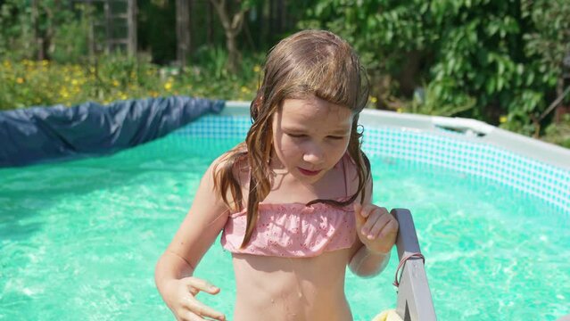 Cute teenage girl in pink swimsuit playing in a small pool. 