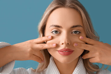 Young woman doing face building exercise on blue background, closeup