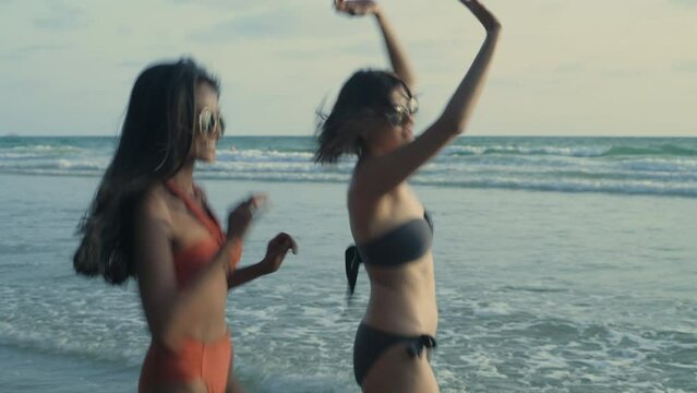 Holiday concept of 4k Resolution. Two Asian women in bikinis are dancing on the beach.