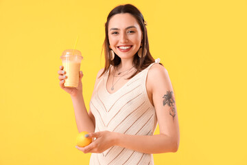 Young woman with glass of smoothie and lemon on yellow background
