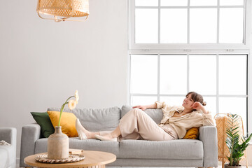 Happy young woman lying on grey sofa in interior of light living room