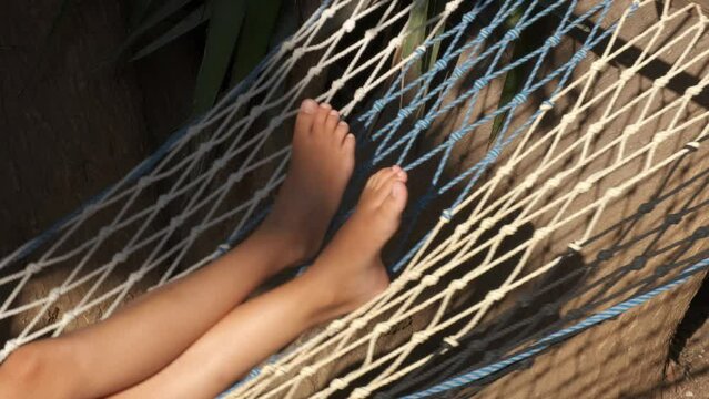 A young girl lies barefoot in a hammock.
