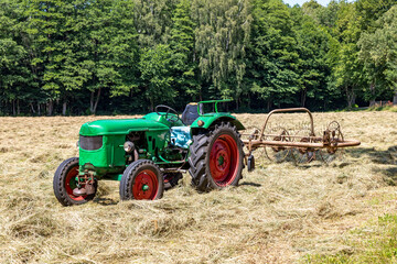 Old farm tractor turning over mowed grass in a meadow. Spring season.