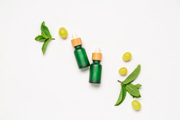 Composition with bottles of essential oil, grapes and mint isolated on white background