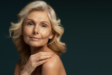 Beautiful mature woman applying anti aging cream and looking at camera
