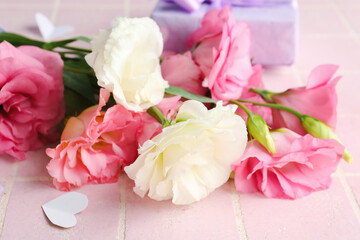 Bouquet of beautiful pink eustoma flowers and gift box on light tile background