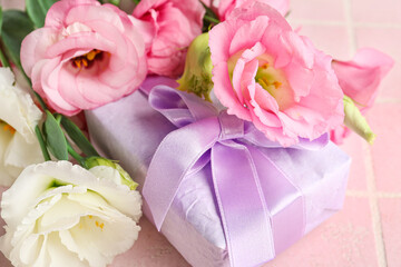 Bouquet of beautiful pink eustoma flowers and gift box on light tile background