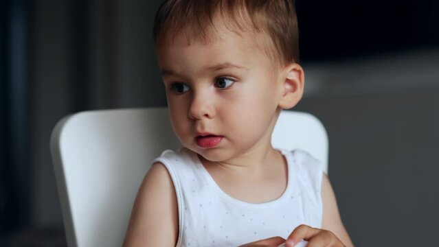 Adorable Caucasian toddler tries to open white plastic egg. Cute child plays at home. Close up.
