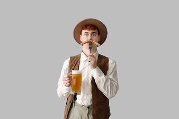 Young man in traditional German clothes with beer and sausage on light background