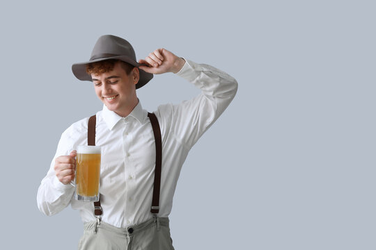 Young man in traditional German clothes with beer on light background