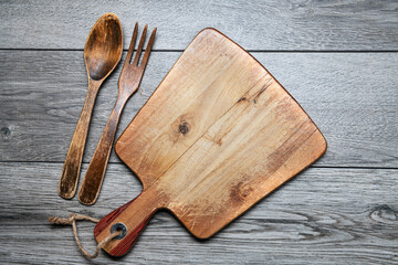 wooden cutting board and wooden spoon and fork on a gray table. View from above. copy space,