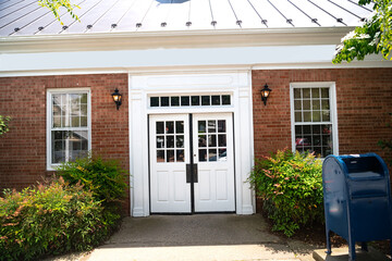 Entrance door to a large brick house. White double door and bushes at the entrance.