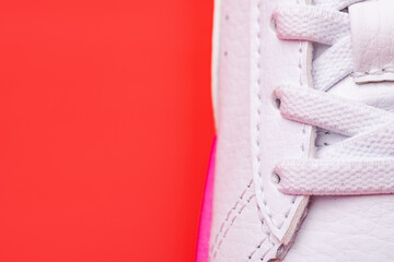 Laced fastening of new sports shoe close-up. Elastic laces of modern textile trainers for active lifestyle, sport, and fitness on red background. Copy space.